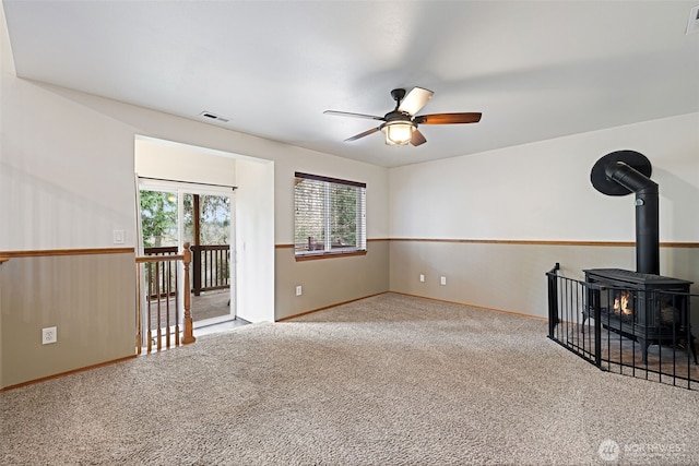 carpeted empty room featuring visible vents, a wood stove, and ceiling fan