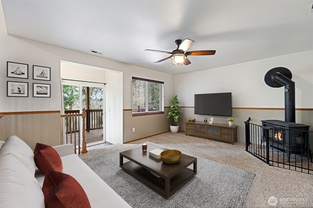 carpeted living room with visible vents, a ceiling fan, and a wood stove