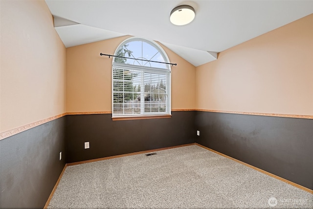 carpeted empty room with visible vents, baseboards, and lofted ceiling