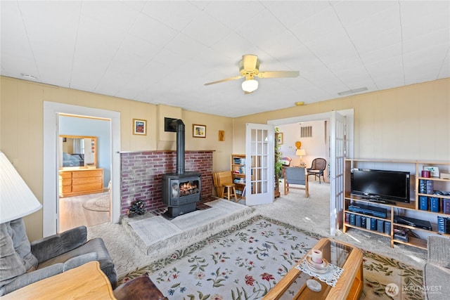 carpeted living area featuring french doors, ceiling fan, and a wood stove