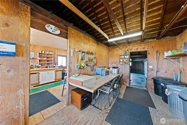 dining room with beam ceiling, wood walls, a workshop area, and wood finished floors