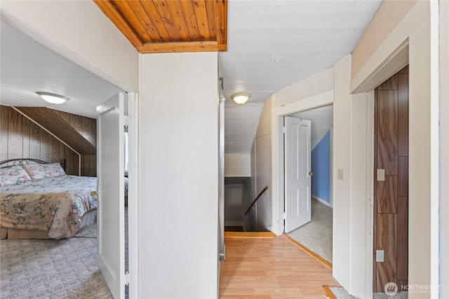 corridor featuring light wood-style flooring, an upstairs landing, and wood walls