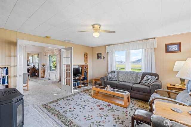 living room with a ceiling fan, a wood stove, carpet flooring, and french doors