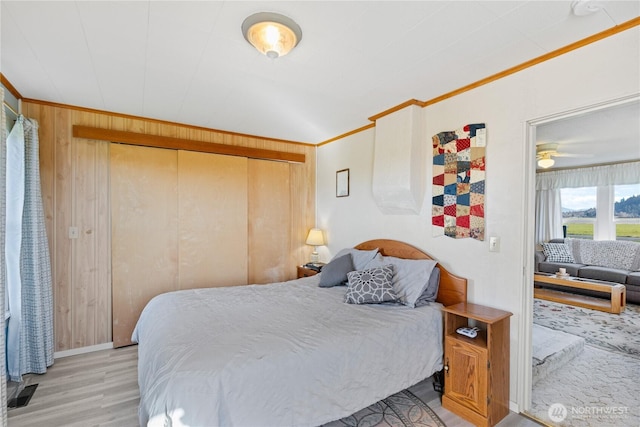 bedroom with a closet, wooden walls, light wood-type flooring, and crown molding