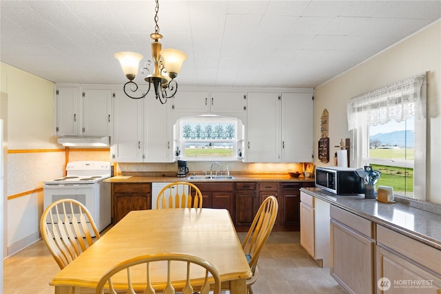 kitchen with under cabinet range hood, pendant lighting, a notable chandelier, white appliances, and a sink