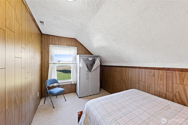 bedroom with visible vents, light carpet, a textured ceiling, wood walls, and vaulted ceiling