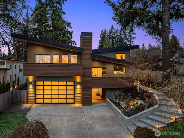 contemporary house with a garage, a chimney, driveway, and fence