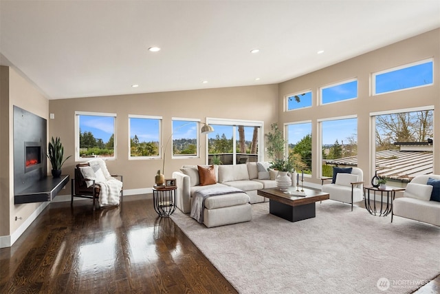 living area with wood finished floors, baseboards, high vaulted ceiling, recessed lighting, and a glass covered fireplace