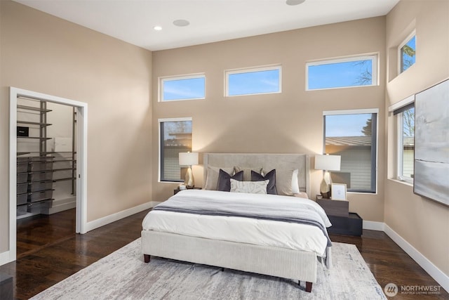 bedroom featuring wood finished floors, baseboards, and a towering ceiling