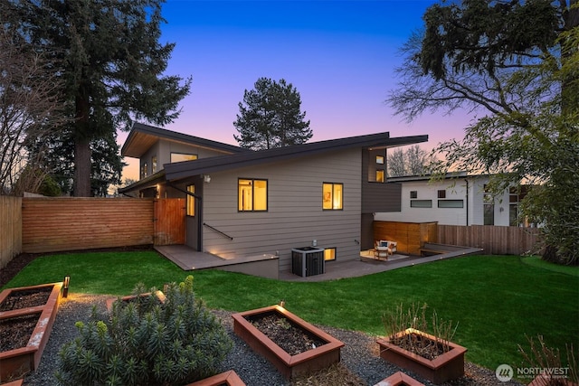 back of house at dusk with central AC, a yard, a vegetable garden, and a fenced backyard