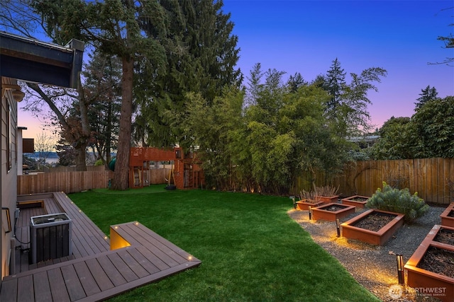 yard at dusk with central AC unit, a playground, a fenced backyard, and a garden