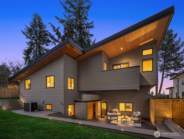 back of property at dusk with a deck, fence, central AC, and an outdoor hangout area