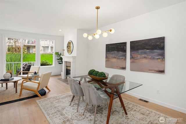 dining area featuring visible vents, a fireplace with flush hearth, light wood finished floors, baseboards, and a chandelier