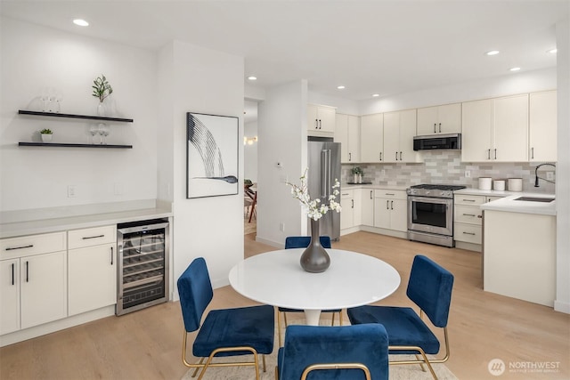 kitchen with beverage cooler, a sink, decorative backsplash, appliances with stainless steel finishes, and exhaust hood