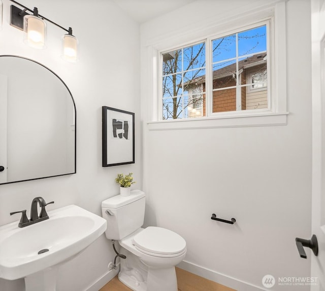 half bathroom with toilet, baseboards, and a sink