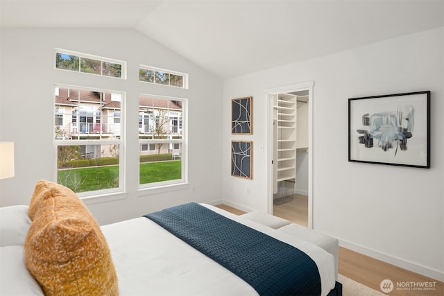 bedroom featuring a walk in closet, lofted ceiling, wood finished floors, and baseboards