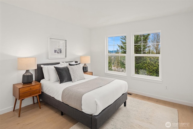 bedroom with light wood finished floors, visible vents, and baseboards