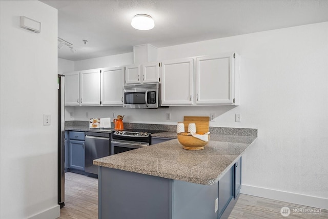 kitchen with white cabinetry, a peninsula, light wood-style flooring, and stainless steel appliances