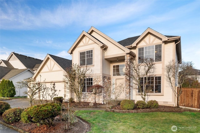 traditional-style house with a garage, stone siding, a front lawn, and fence