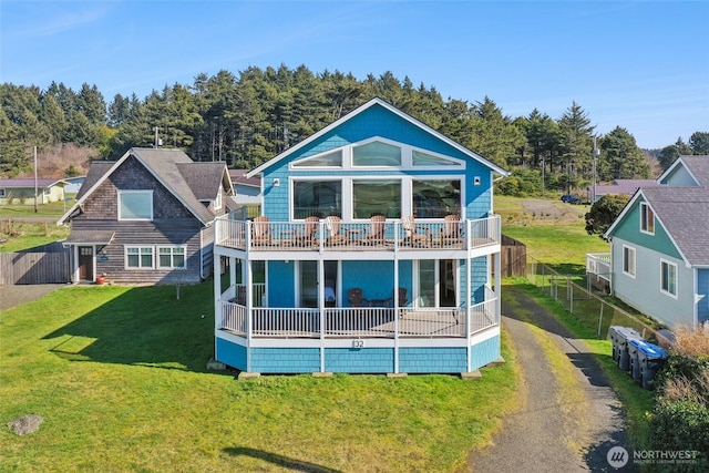 rear view of property featuring a lawn, a balcony, driveway, and fence