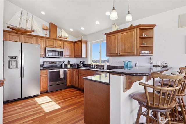 kitchen with a peninsula, a sink, stainless steel appliances, decorative light fixtures, and brown cabinets