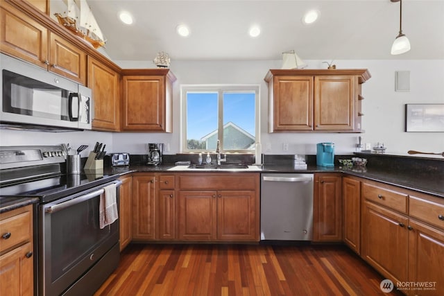 kitchen featuring dark countertops, dark wood finished floors, appliances with stainless steel finishes, brown cabinetry, and a sink