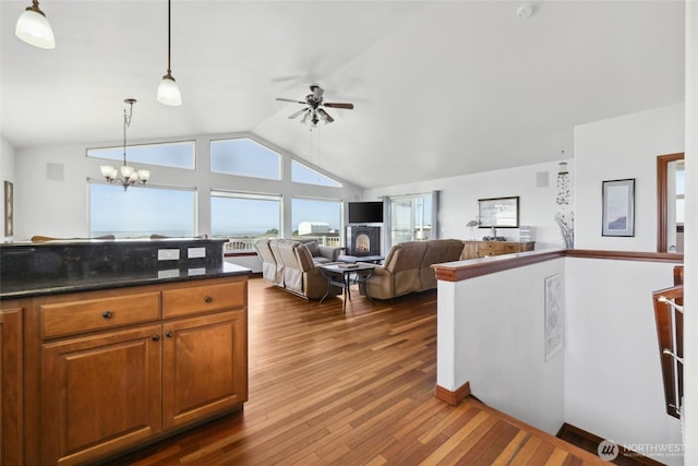 kitchen with pendant lighting, lofted ceiling, ceiling fan with notable chandelier, brown cabinetry, and dark wood-style flooring