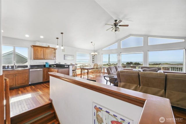 kitchen with pendant lighting, vaulted ceiling, ceiling fan with notable chandelier, stainless steel dishwasher, and dark wood-style flooring