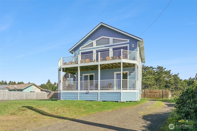 back of property with a balcony, a yard, fence, and driveway