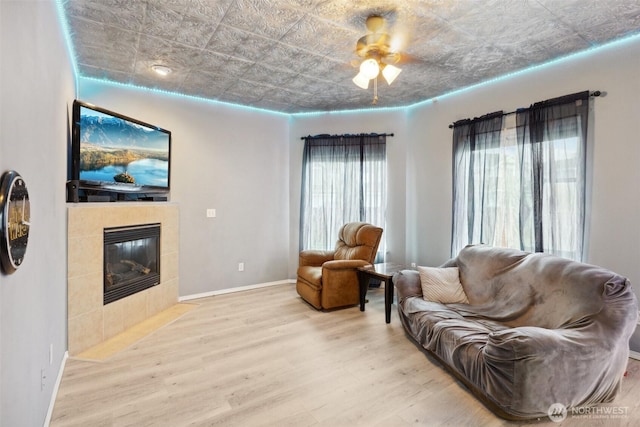 living area featuring baseboards, a tile fireplace, wood finished floors, an ornate ceiling, and a ceiling fan