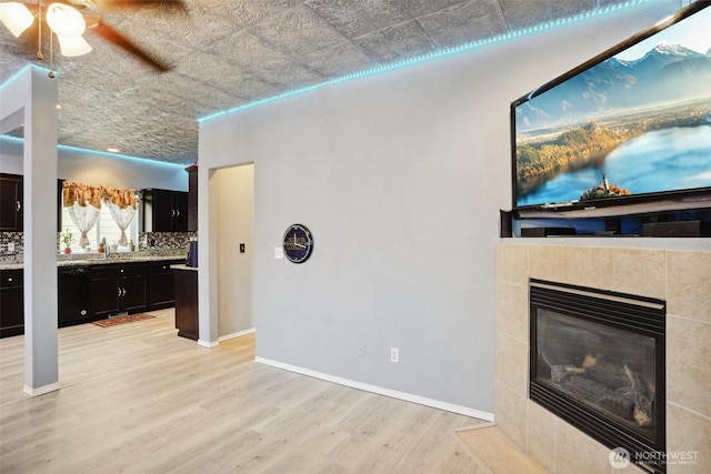 living room with light wood-style flooring, a fireplace, baseboards, and an ornate ceiling