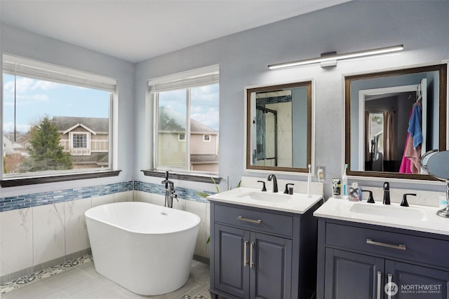 bathroom with a freestanding tub, two vanities, wainscoting, and a sink