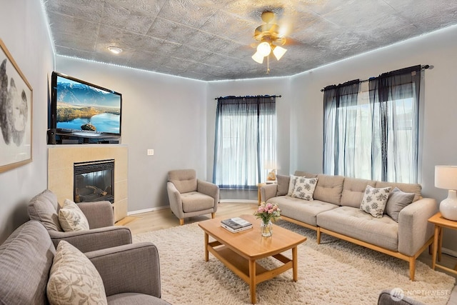 living room with ceiling fan, wood finished floors, baseboards, and a tile fireplace