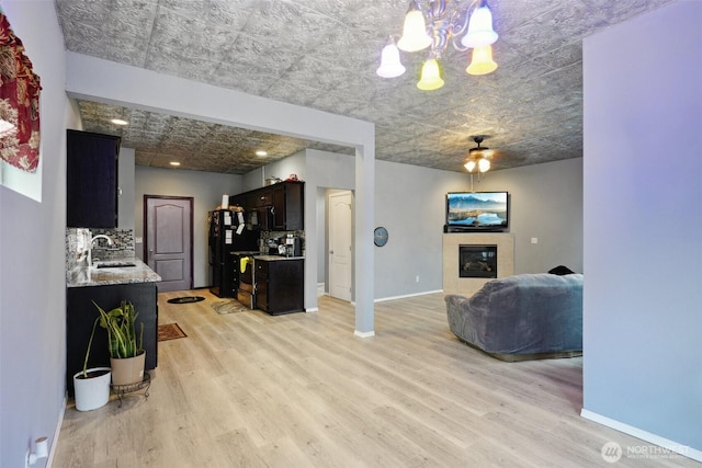 living area with light wood-type flooring, baseboards, a tiled fireplace, and ceiling fan with notable chandelier