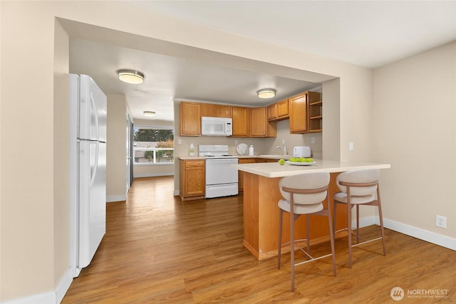 kitchen with white appliances, a peninsula, wood finished floors, and light countertops