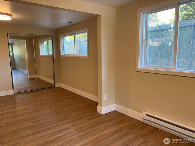 unfurnished bedroom featuring a closet, a baseboard heating unit, baseboards, and wood finished floors