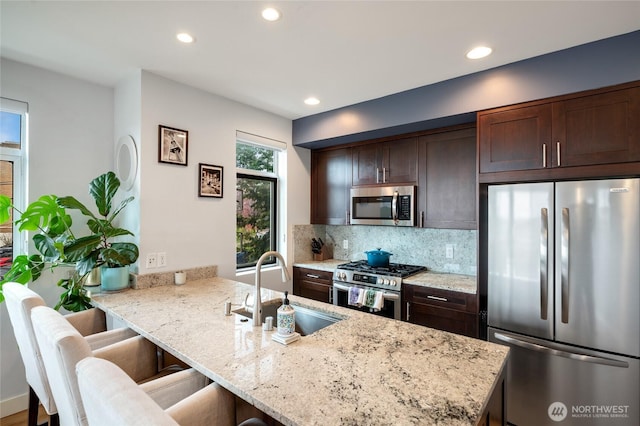 kitchen with dark brown cabinets, decorative backsplash, appliances with stainless steel finishes, a kitchen breakfast bar, and a sink