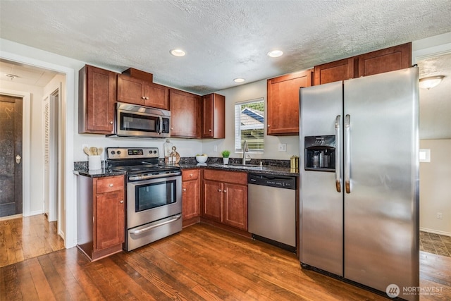 kitchen with a sink, a textured ceiling, recessed lighting, appliances with stainless steel finishes, and dark wood-style flooring