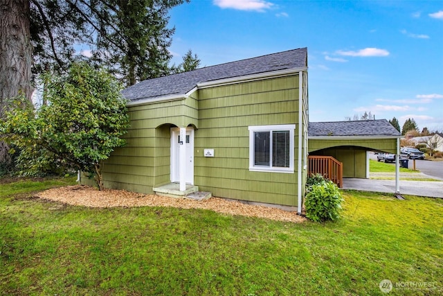 rear view of property featuring a yard, a carport, roof with shingles, and driveway