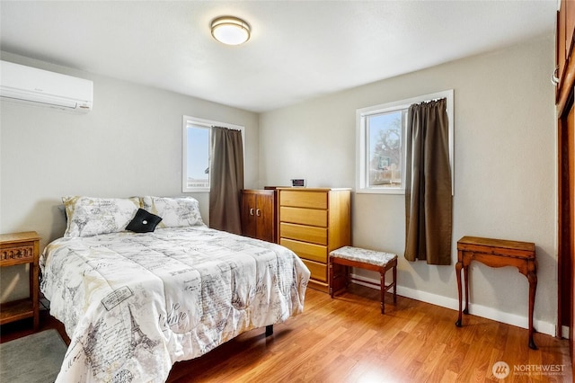 bedroom with a wall unit AC, multiple windows, light wood-style floors, and baseboards