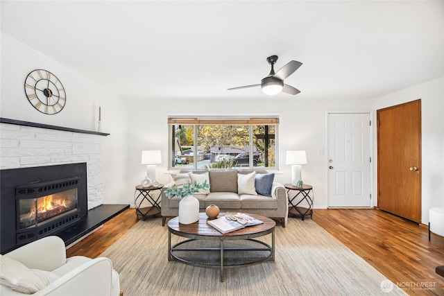 living area with a glass covered fireplace, a ceiling fan, and wood finished floors