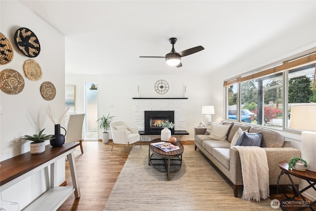 living area featuring a fireplace, a ceiling fan, and wood finished floors