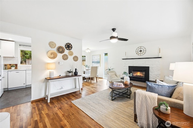 living room featuring a glass covered fireplace, baseboards, a ceiling fan, and wood finished floors