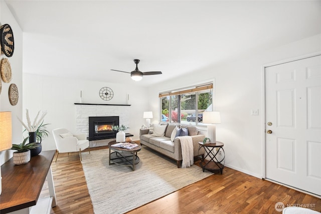 living room featuring ceiling fan, baseboards, wood finished floors, and a fireplace