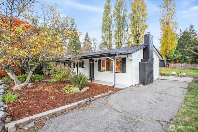 view of front of home with covered porch, driveway, a chimney, and fence