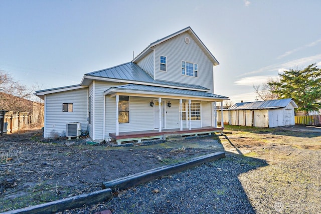 view of front facade featuring central AC, covered porch, metal roof, a storage shed, and an outbuilding