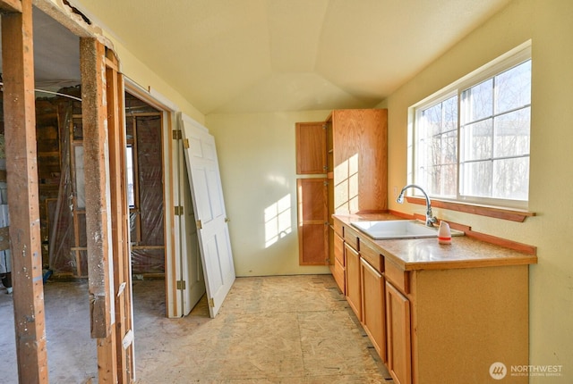 kitchen featuring brown cabinetry, light countertops, lofted ceiling, and a sink