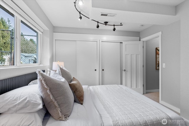 bedroom with visible vents, rail lighting, two closets, and baseboards