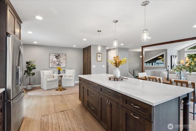 kitchen with light wood-type flooring, a kitchen bar, recessed lighting, stainless steel fridge, and dark brown cabinets