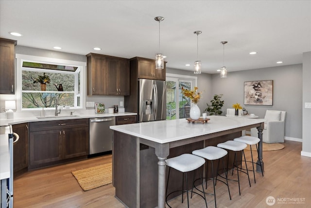 kitchen with dark brown cabinets, stainless steel appliances, light wood-style floors, and a sink